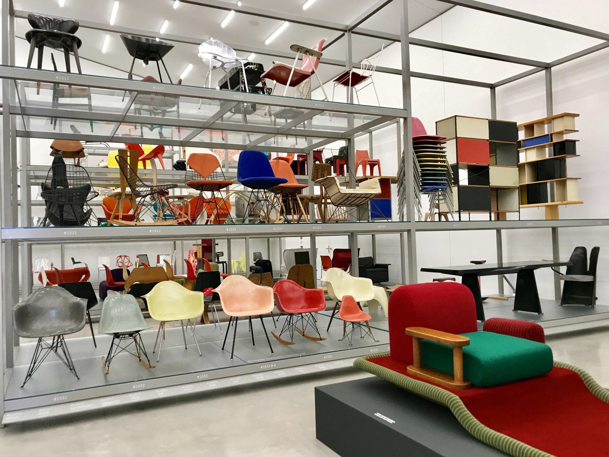 Sur l'étagère sont exposées les "molded wood chairs", "fiberglass armchairs" et "wire chairs" du couple Eames